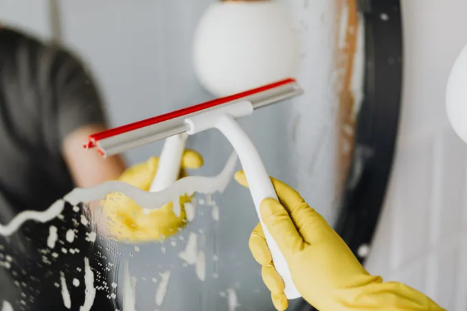 A gloved hand cleaning glass with a squeegee — illustrative stock photograph